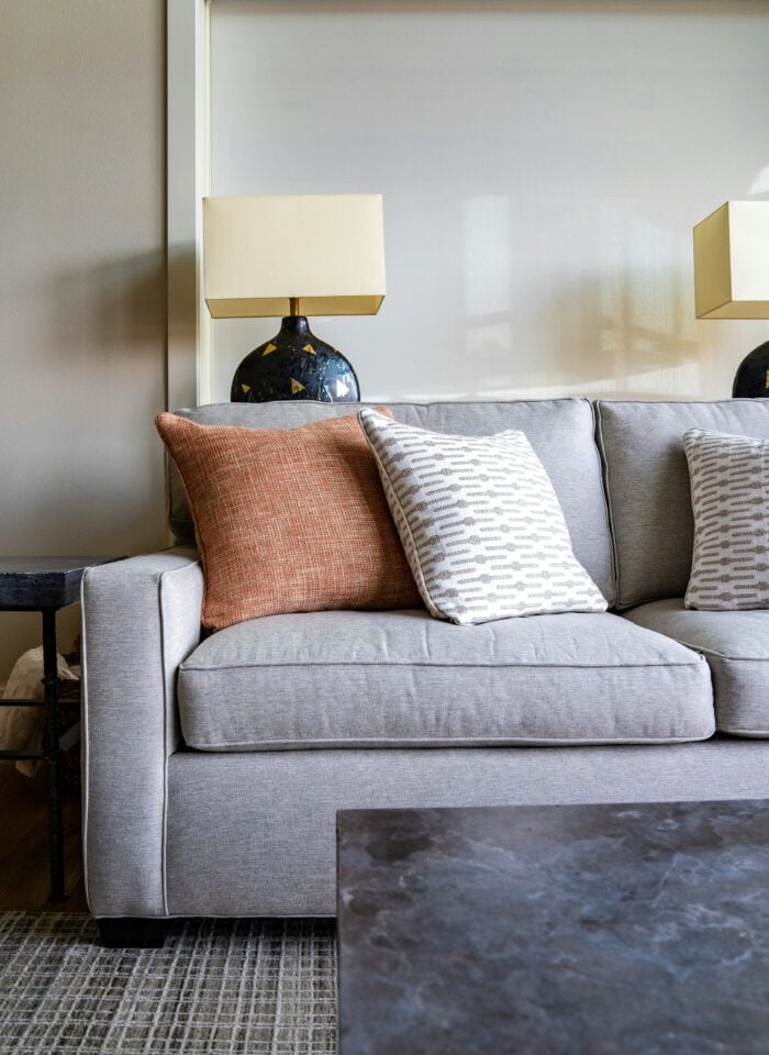 Modern living room with grey fabric sofa, decorative throw pillows, table lamps and neutral decor, cozy minimalist interior design with soft textures and warm lighting.