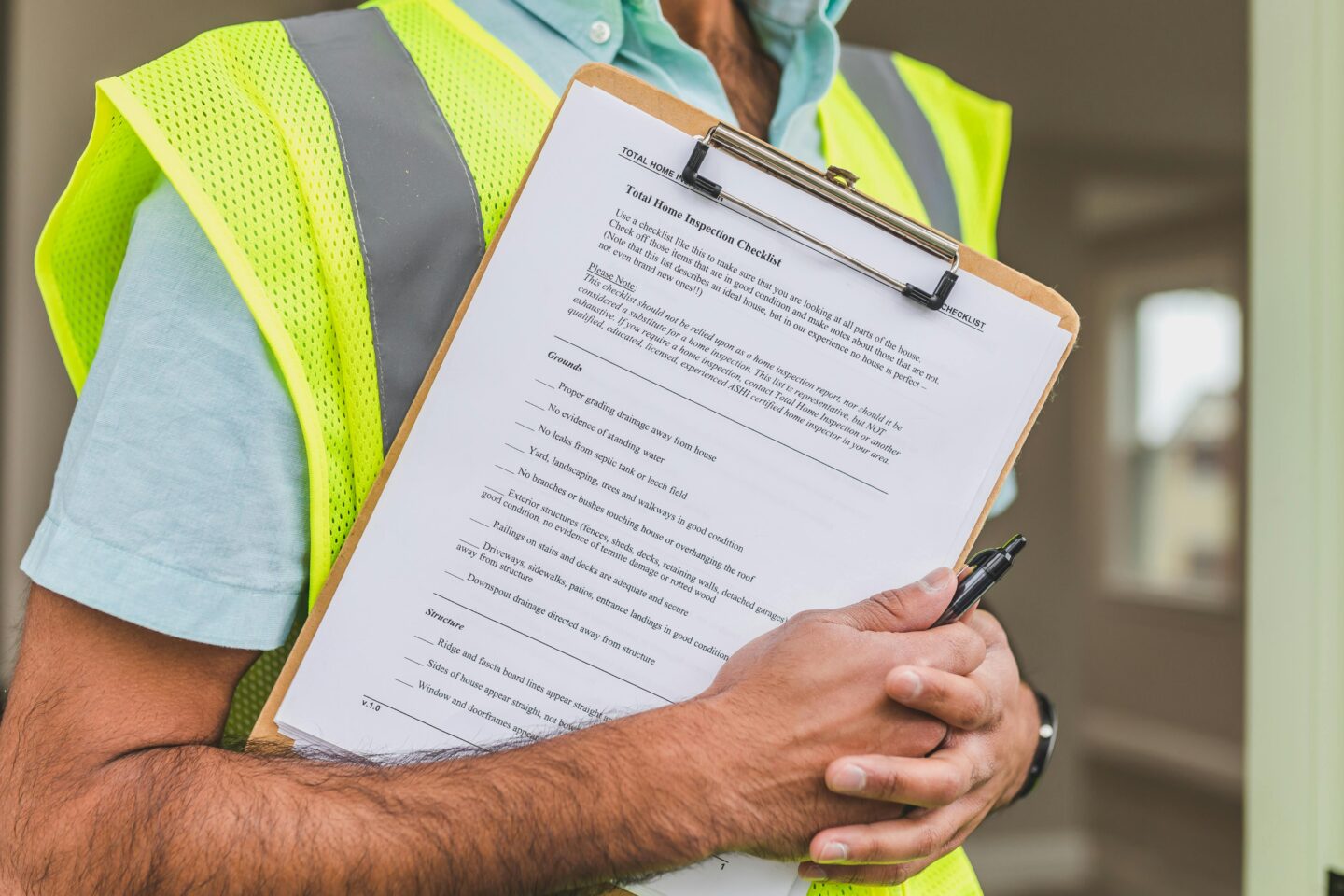 Home inspector wearing a high-visibility vest holding a clipboard with a property inspection checklist.