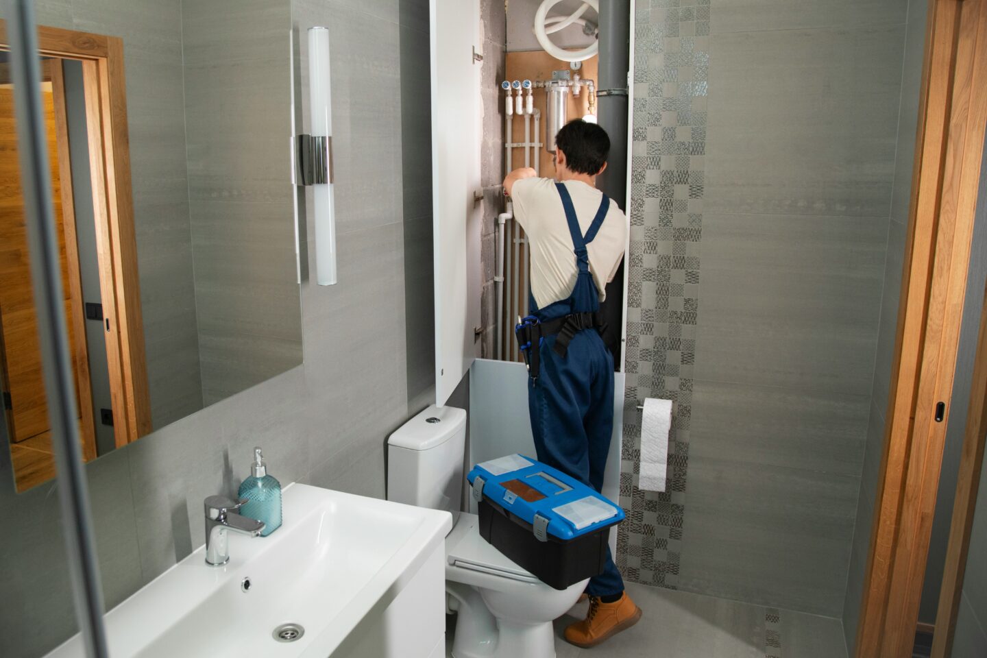 Plumber repairing exposed pipes behind a bathroom wall with tools nearby.