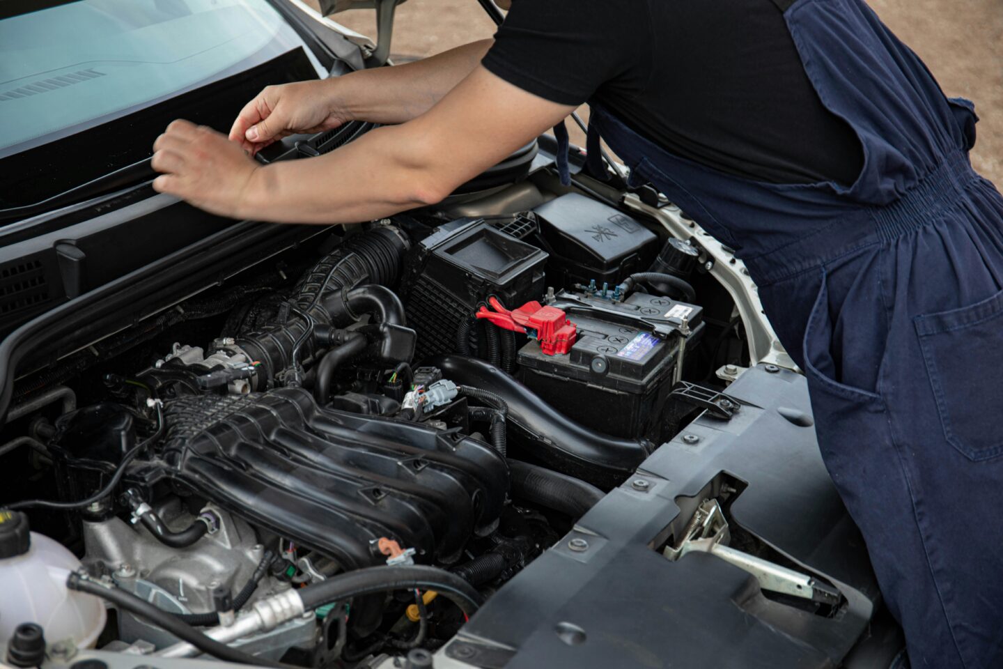 Mechanic working under the hood of a car checking the engine and battery.