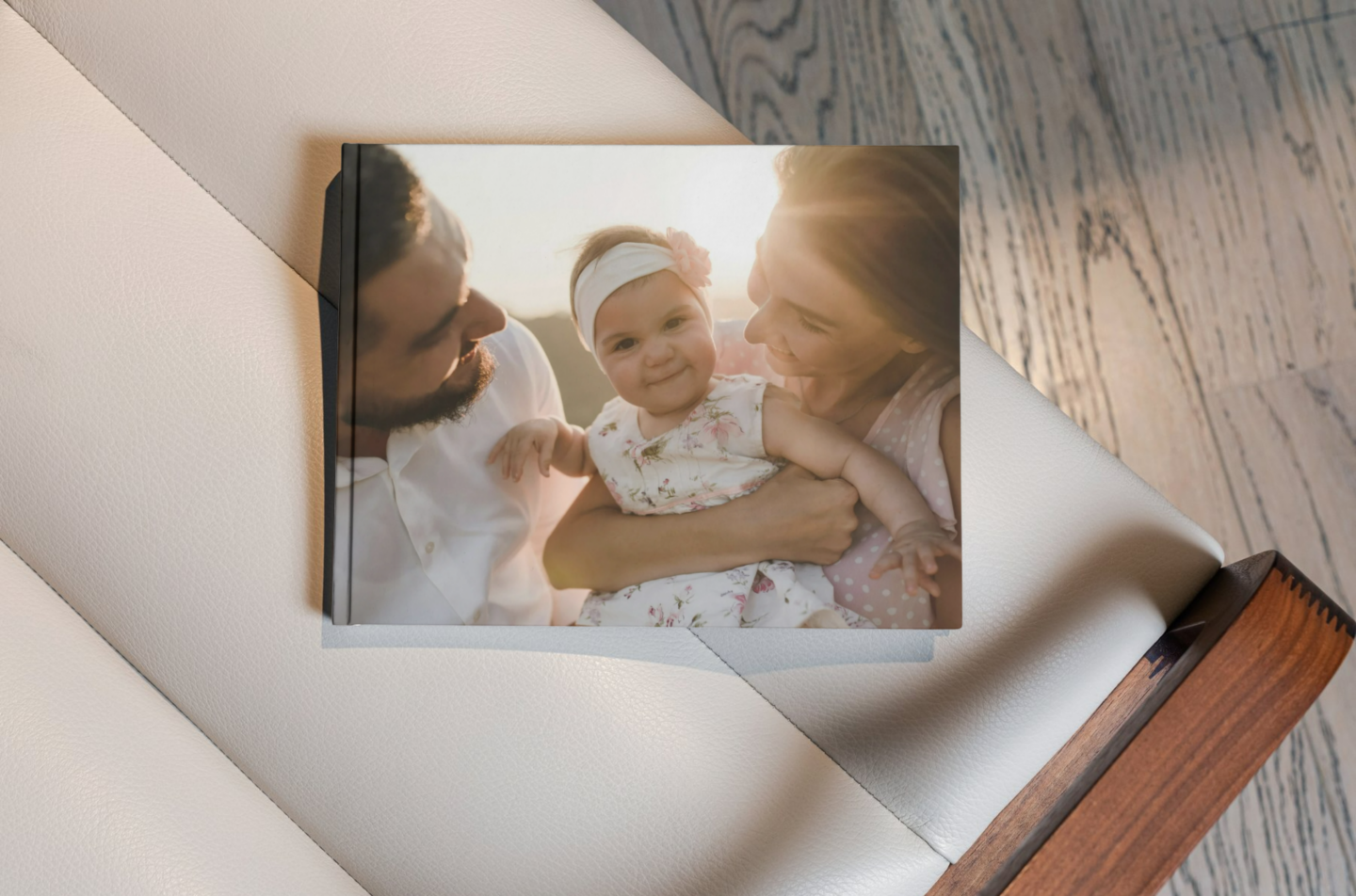 Photobook with a hardcover featuring a warm, sunlit family portrait of parents holding their smiling baby, resting on a soft leather surface.
