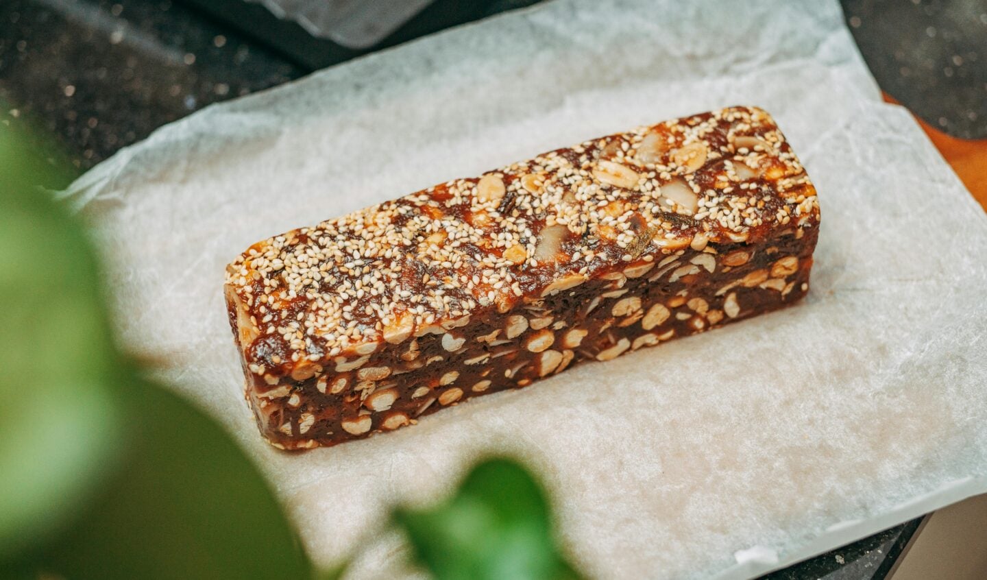 Homemade energy bar with nuts, seeds, and dried fruit on parchment paper, ideal high-calorie snack for hiking lunch ideas.