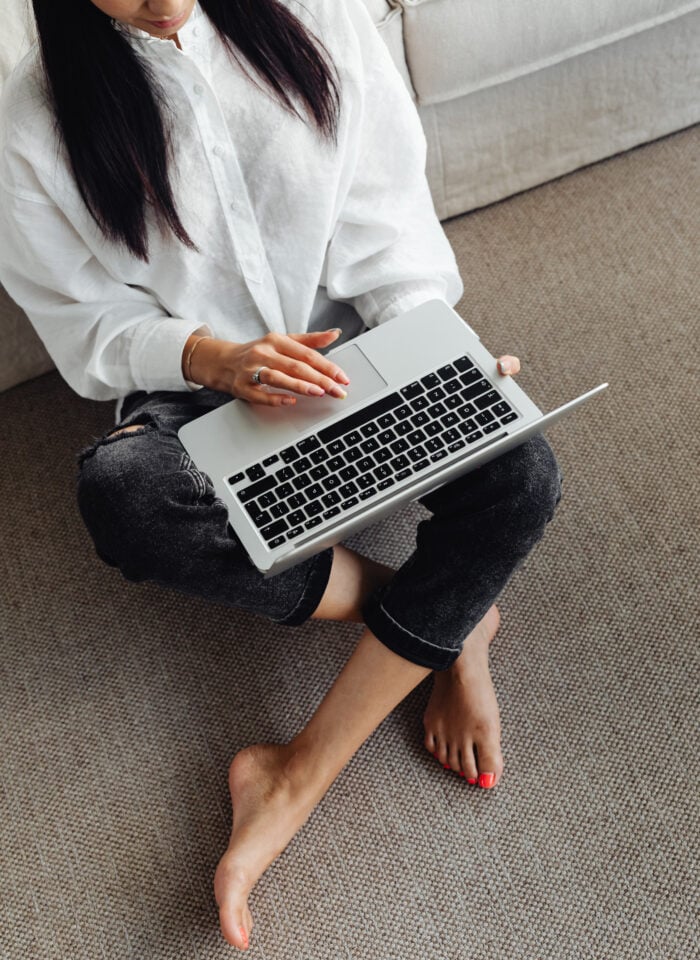 Woman sitting on the floor using a laptop, managing finances or online banking at home in a relaxed setting.