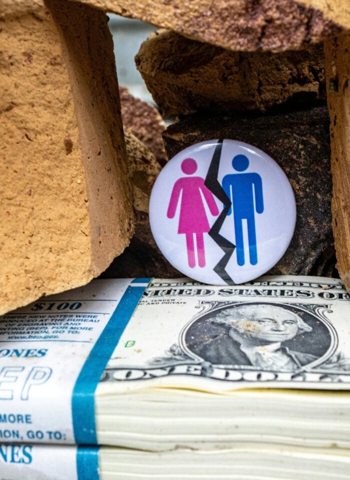Symbolic image of divorce and financial separation with a broken male and female icon placed between bricks above a stack of US dollar bills.