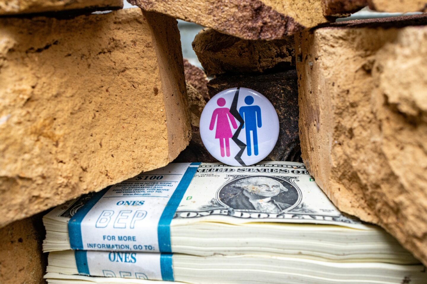 Symbolic image of divorce and financial separation with a broken male and female icon placed between bricks above a stack of US dollar bills.