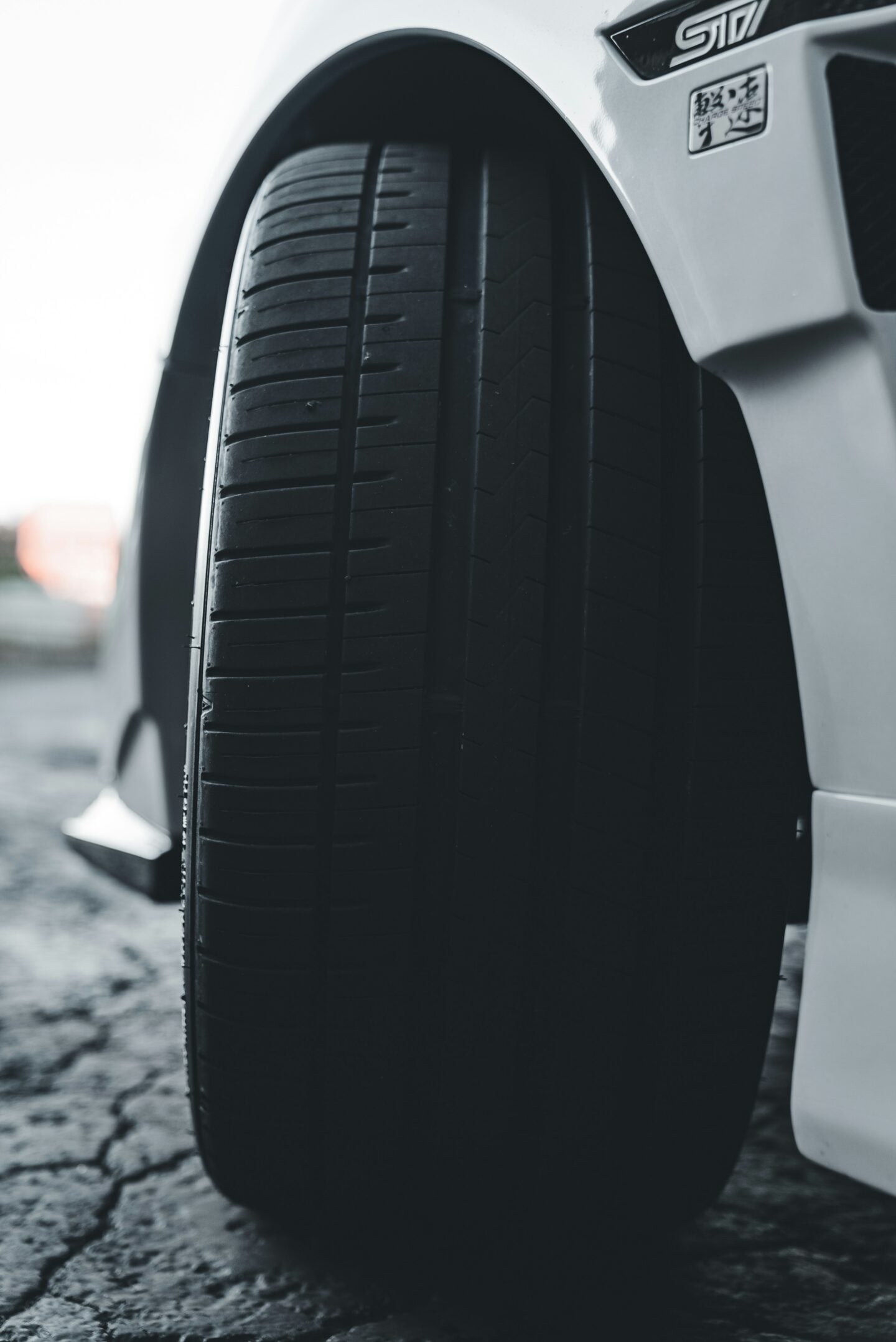 Close-up of a car tire with visible tread on a white vehicle, parked on a textured road surface, highlighting tire condition and performance for driving safety.