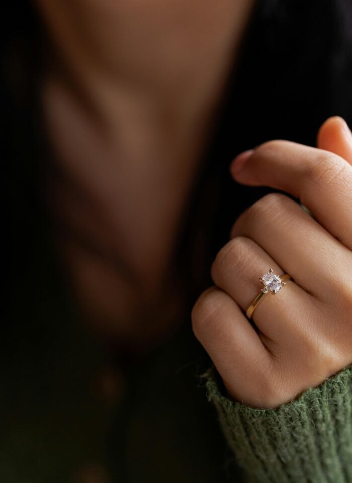 Close-up of a hand wearing a gold solitaire diamond engagement ring with a sparkling center stone.