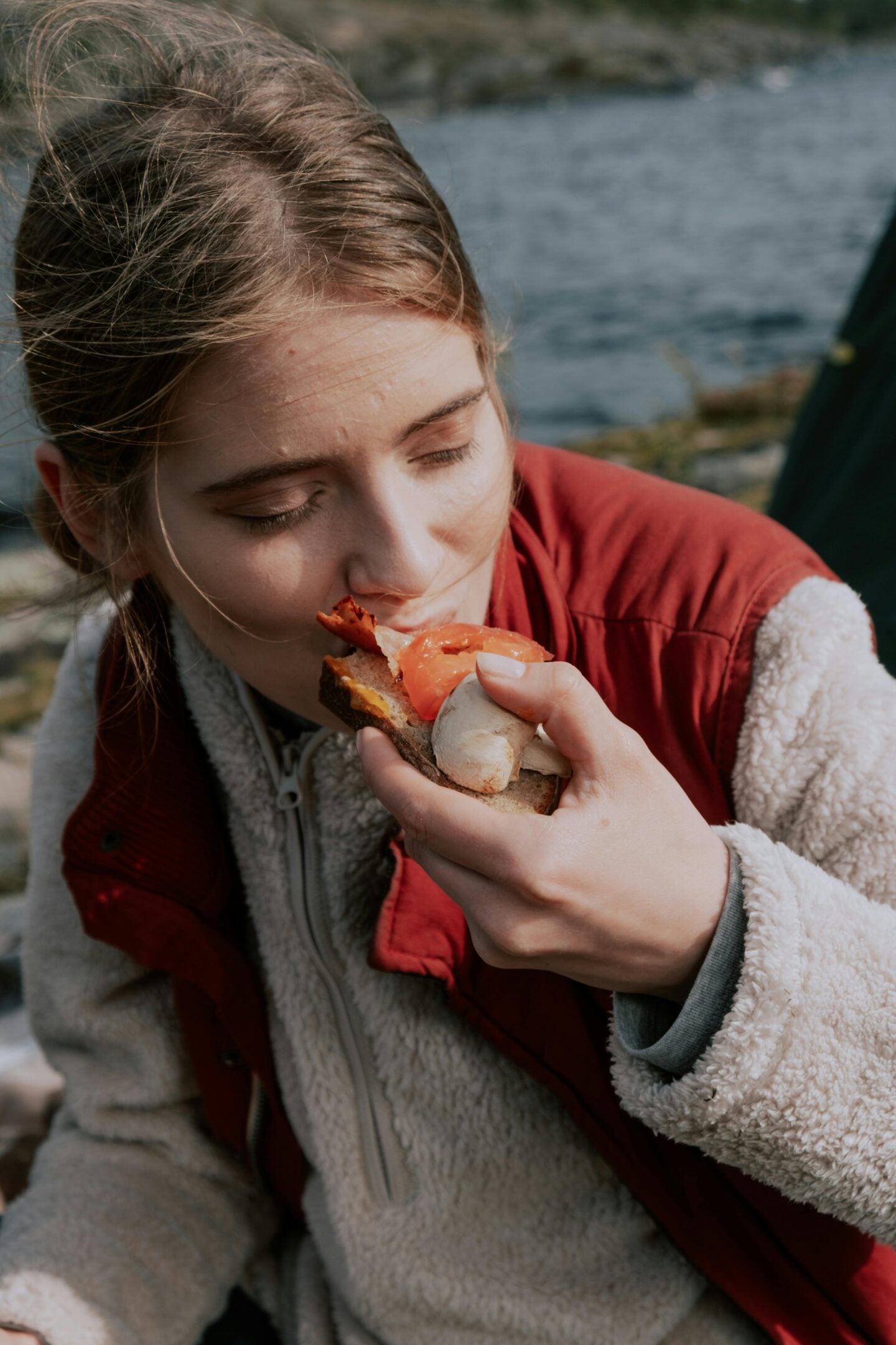 Woman eating sandwich outdoors during hike, example of simple and satisfying hiking lunch ideas on the trail.