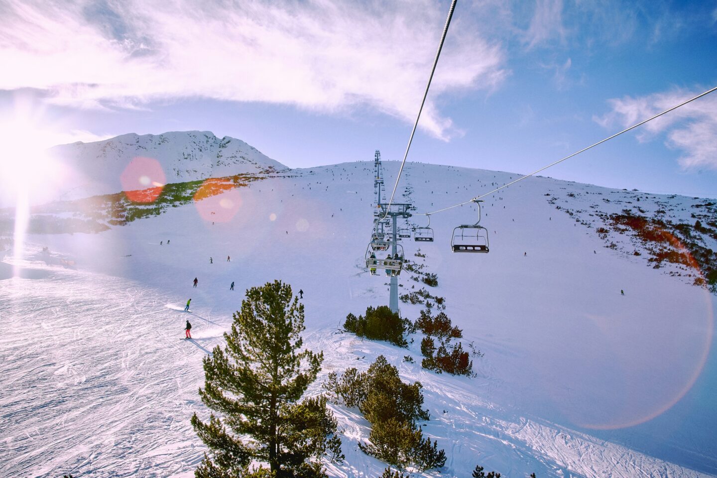 Skiers riding a chairlift and skiing down snowy slopes in Bansko, Bulgaria, on a bright winter day.