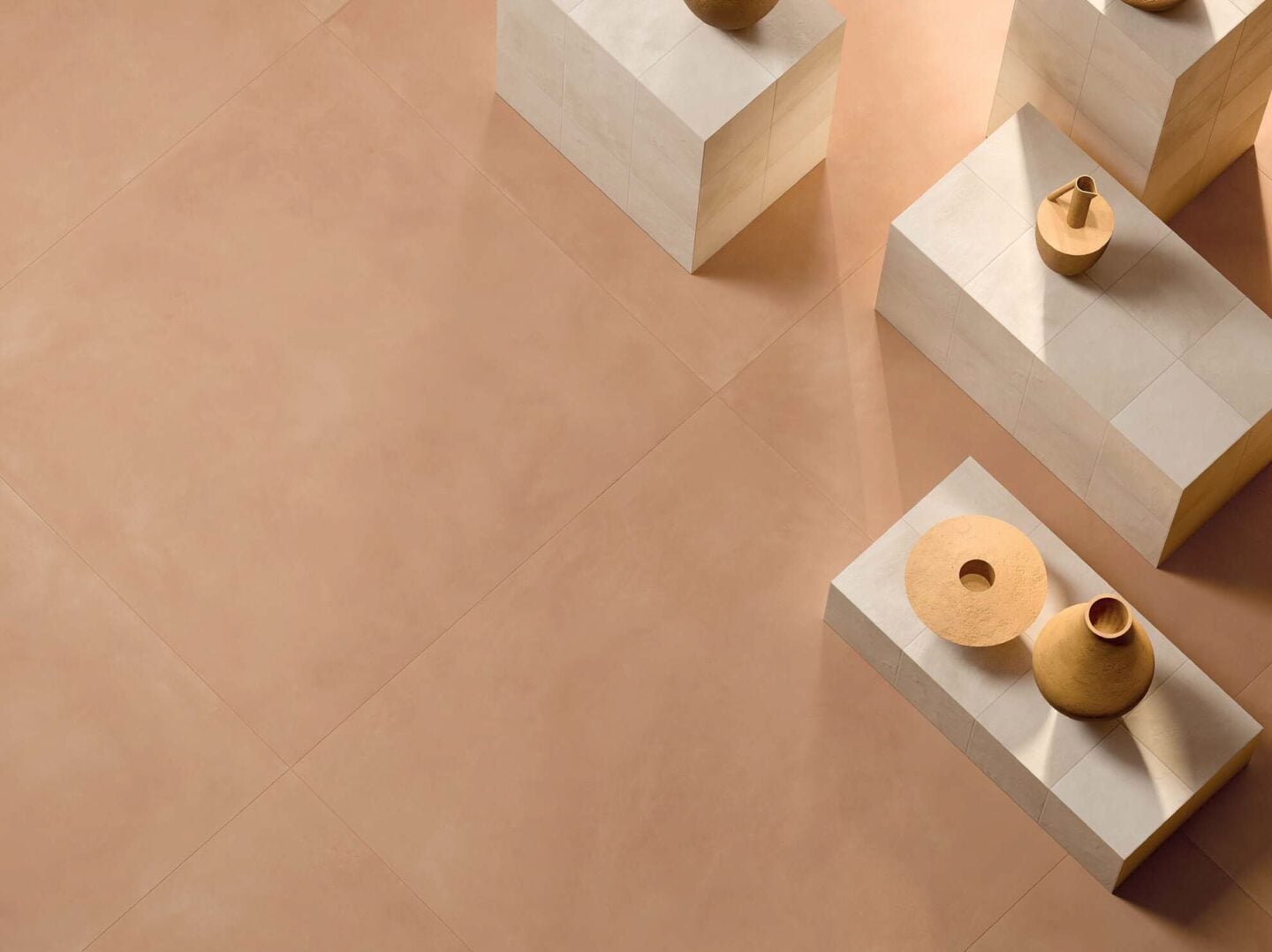 Minimalist interior design featuring warm beige Italian porcelain floor tiles with sculptural ceramic vases displayed on geometric stone pedestals in soft natural light.