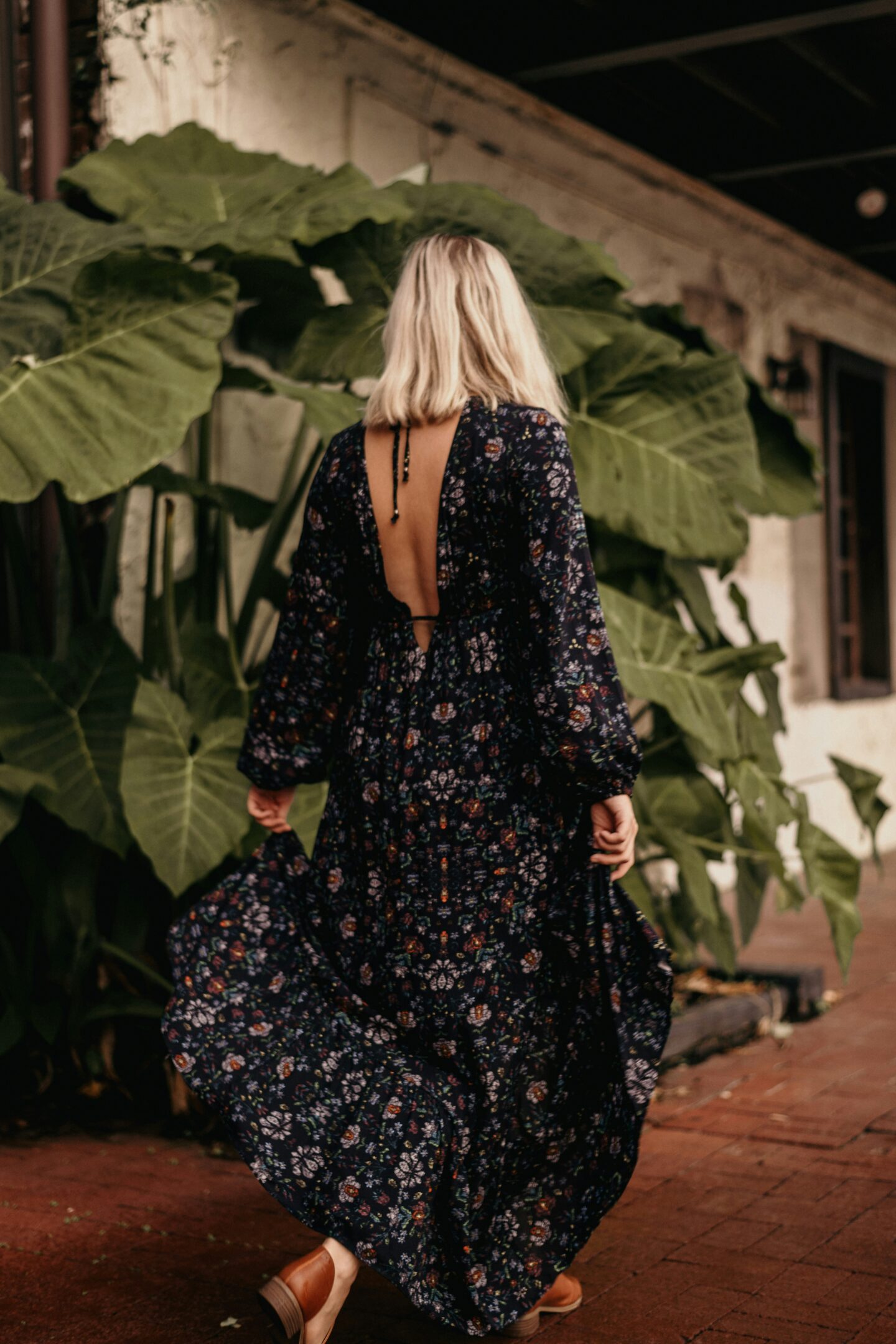 Woman wearing a flowing floral maxi dress with an open back and long sleeves,