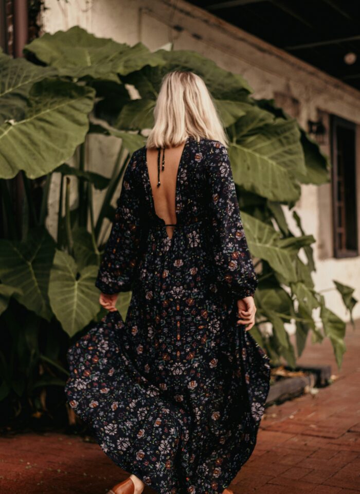 Woman wearing a flowing floral maxi dress with an open back and long sleeves,