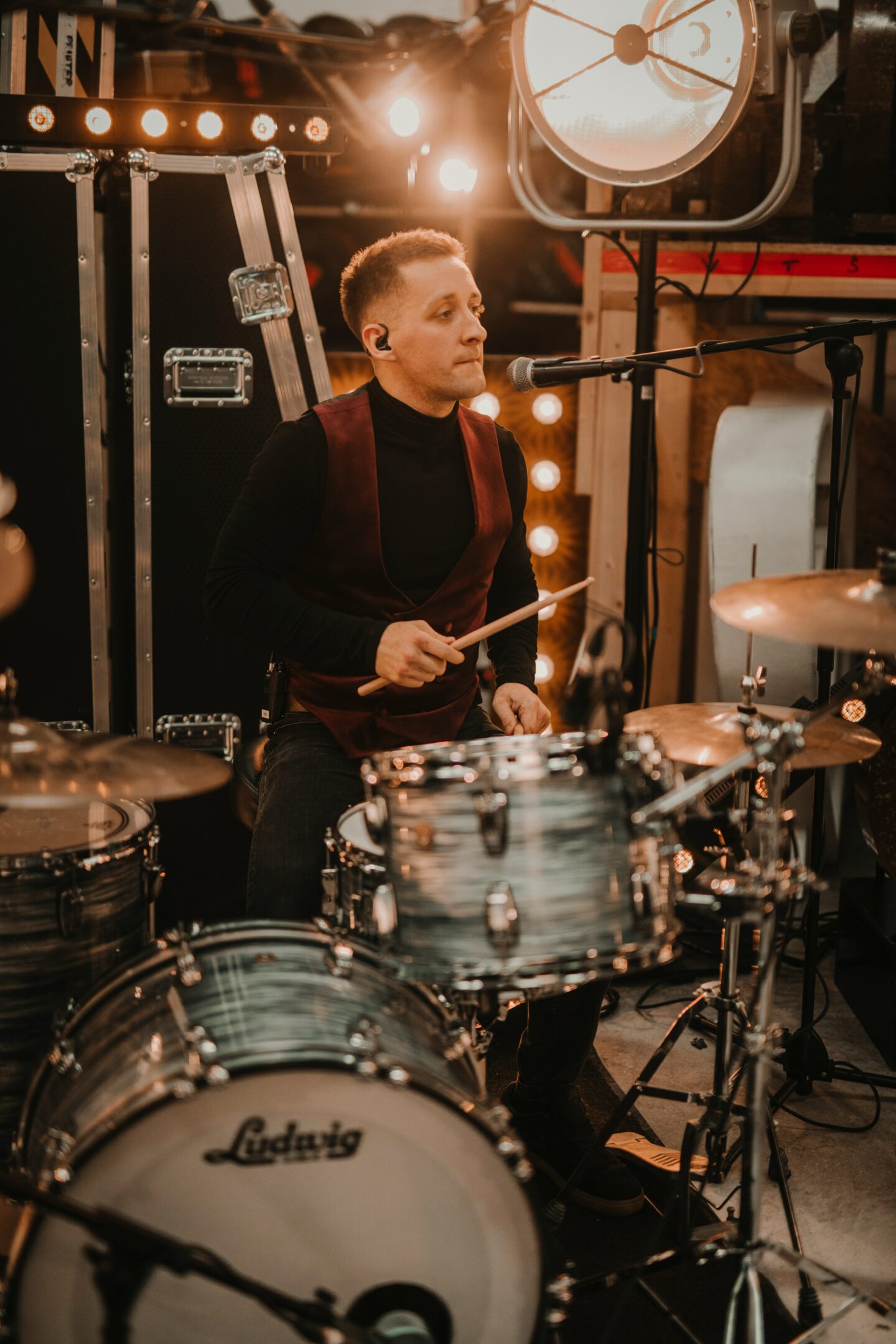Live wedding drummer performing on stage with drum kit and microphone under warm event lighting during an evening wedding reception.