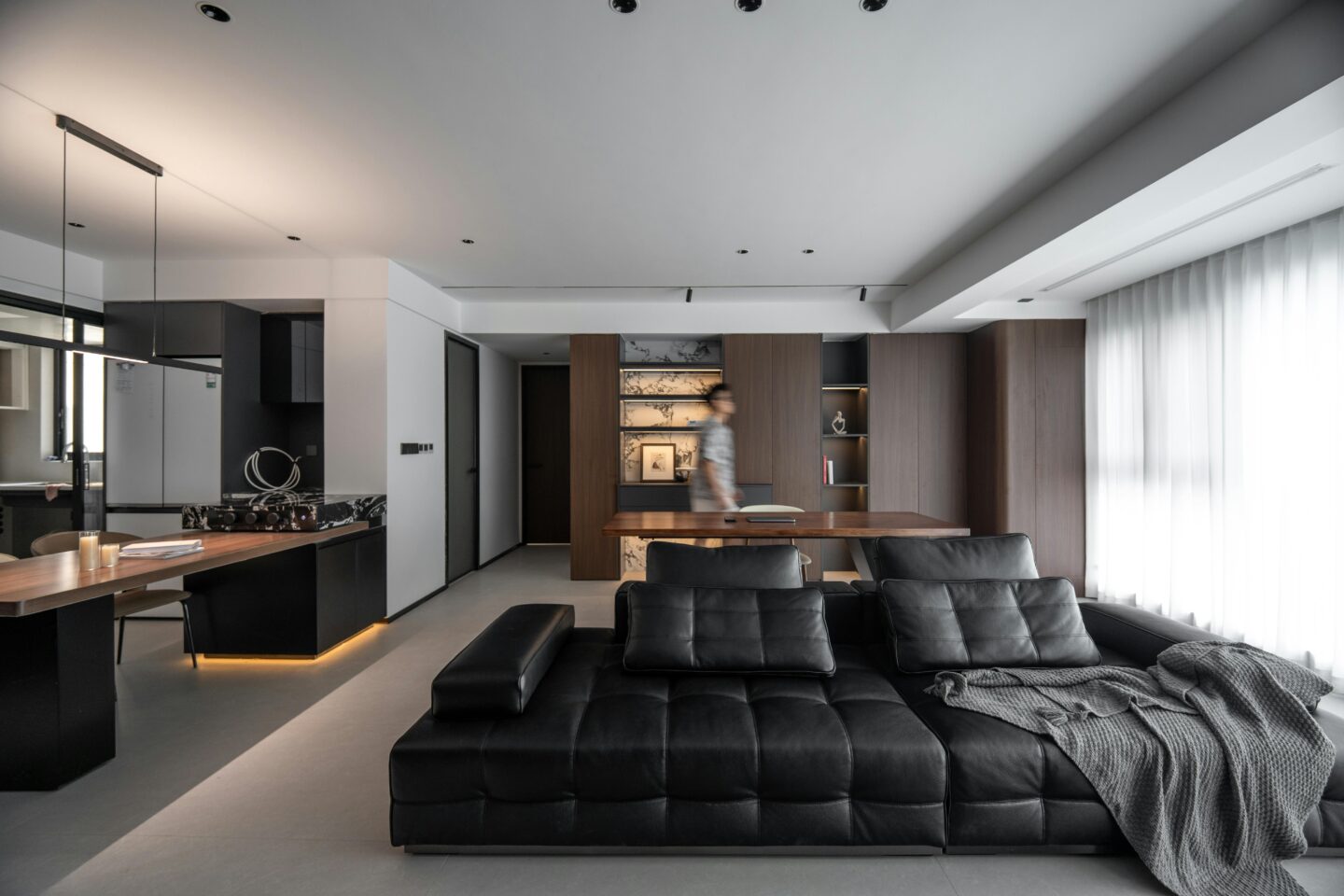 Modern luxury living room with a black tufted sectional sofa as the focal point, surrounded by warm wood finishes, minimalist decor, and an open-plan interior design.