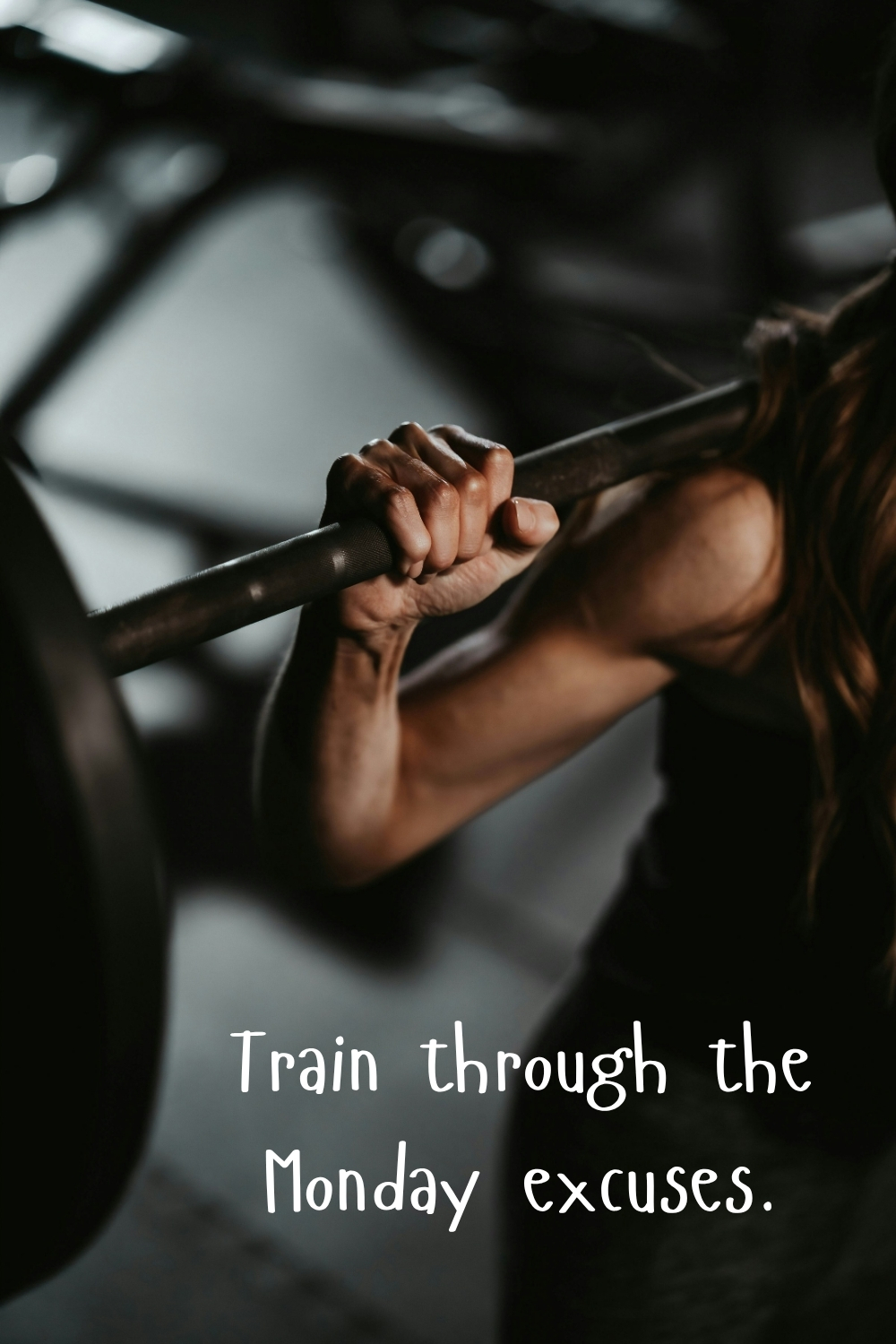 Close-up of a woman lifting a barbell in a dark gym with the quote “Train through the Monday excuses.”