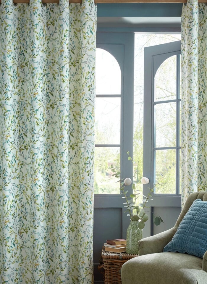 Floral leaf-pattern curtains beside a cushioned armchair and window in a cozy living room with soft natural light.