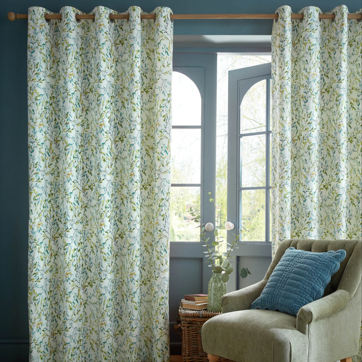 Floral leaf-pattern curtains beside a cushioned armchair and window in a cozy living room with soft natural light.
