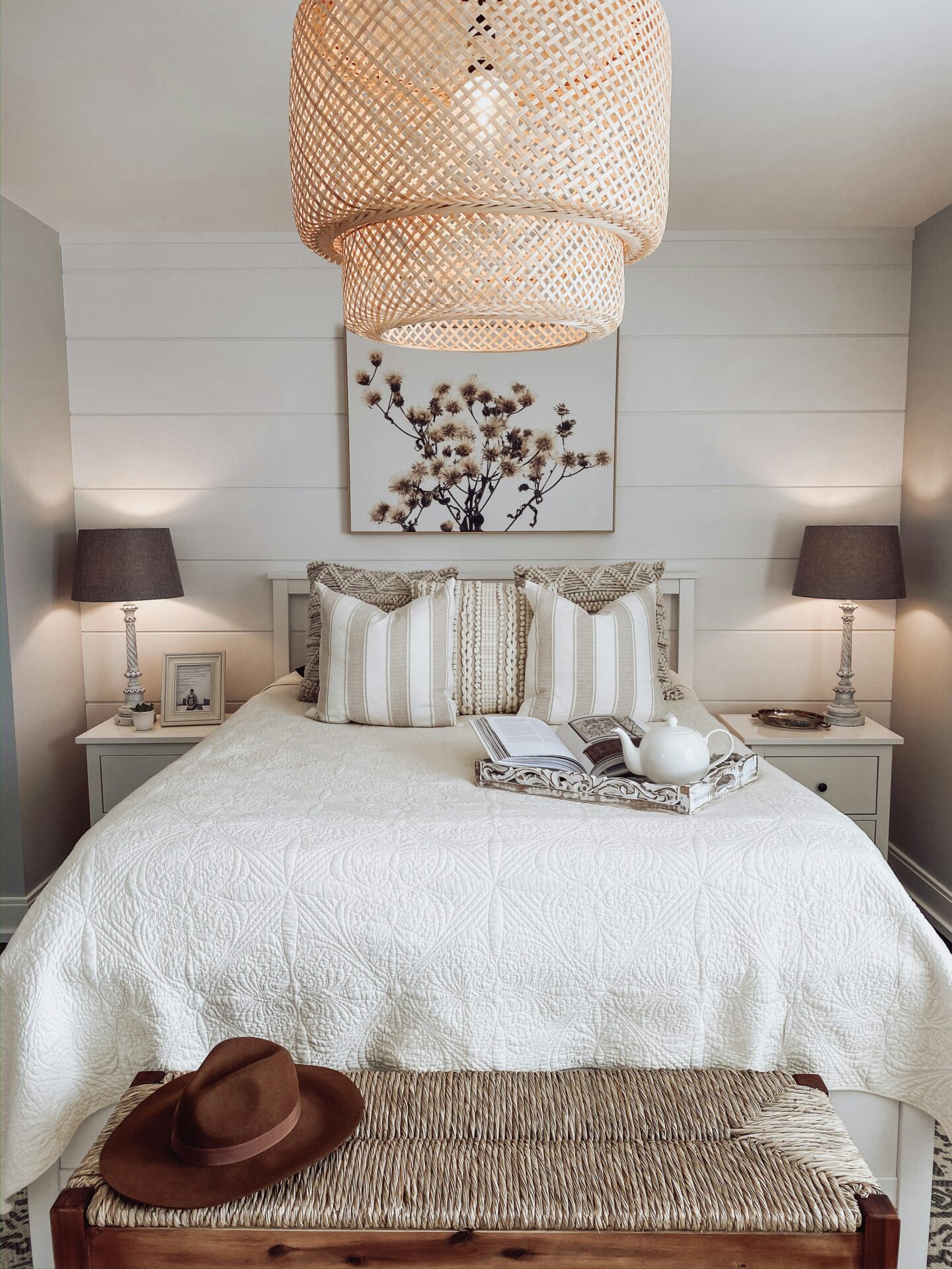 Minimalist neutral bedroom with white quilted bedding, woven pendant light, striped accent pillows, and matching bedside lamps creating a cozy modern farmhouse aesthetic.