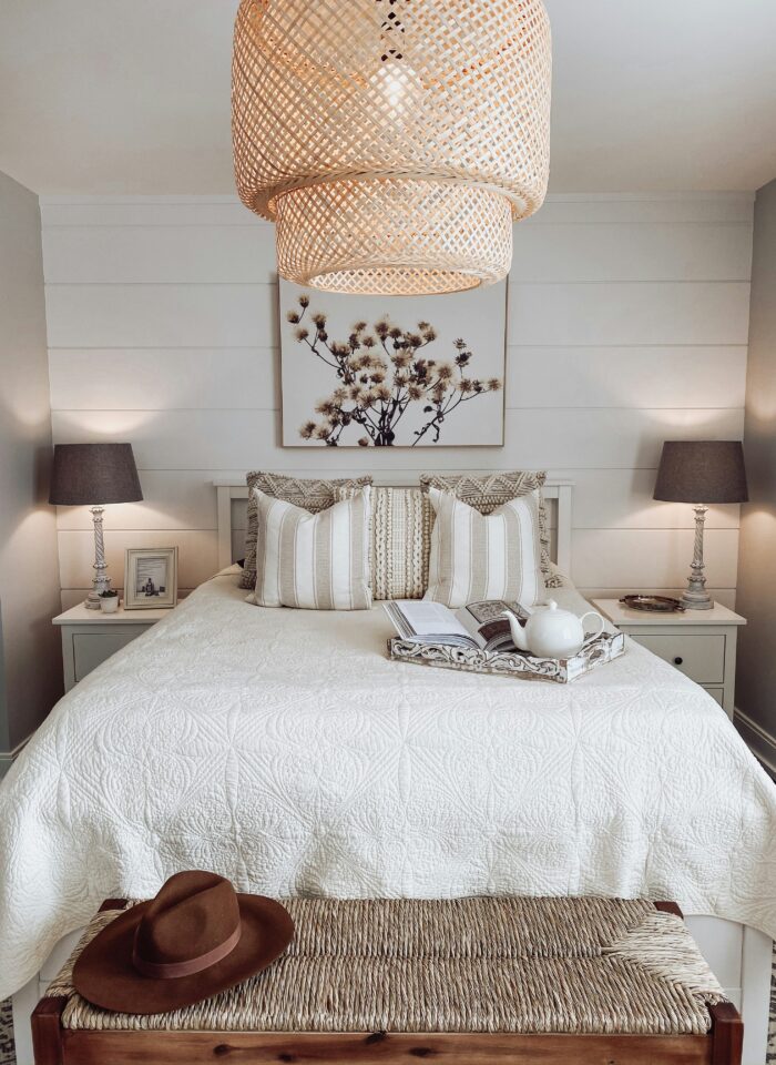 Minimalist neutral bedroom with white quilted bedding, woven pendant light, striped accent pillows, and matching bedside lamps creating a cozy modern farmhouse aesthetic.