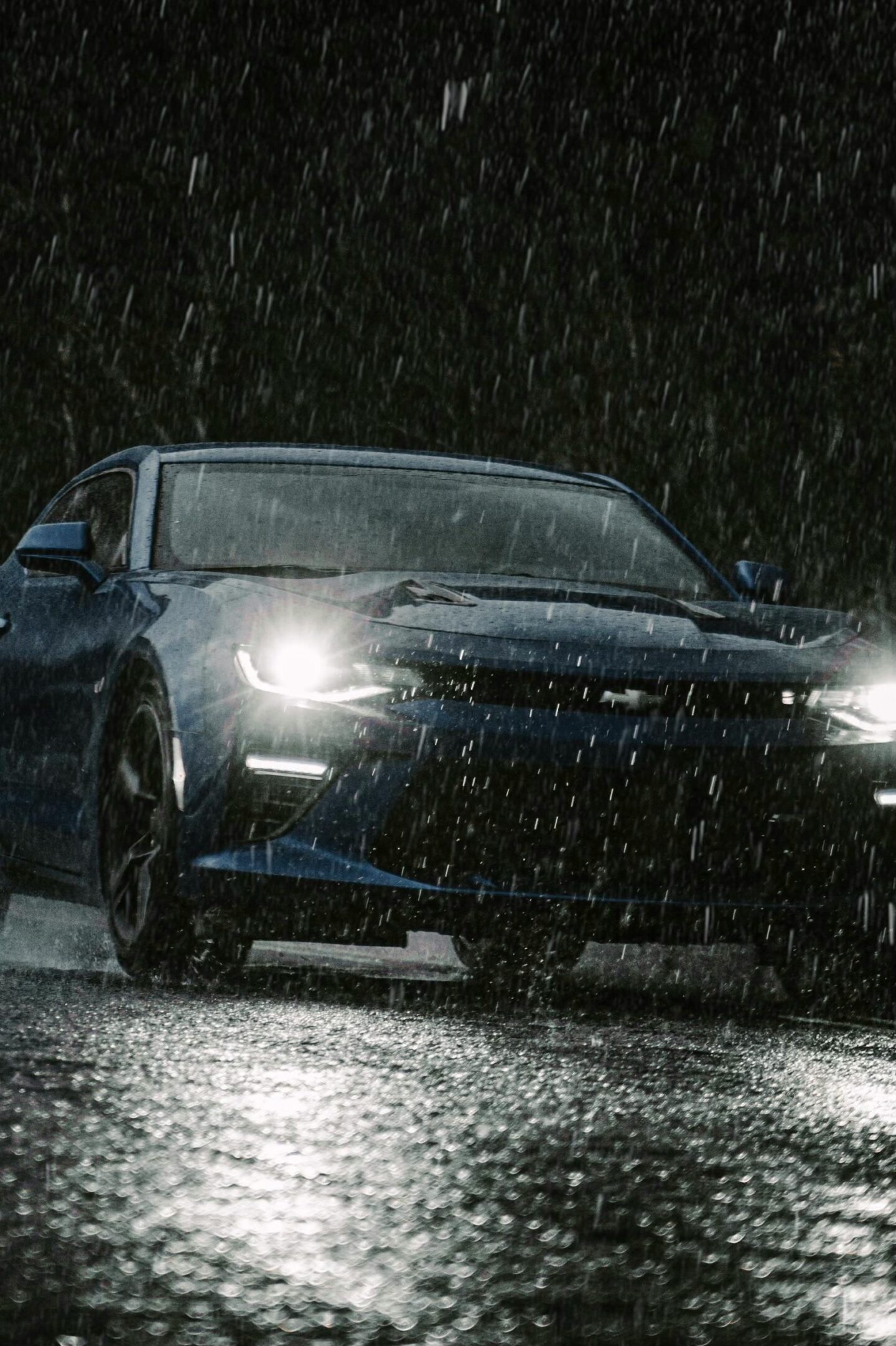 Blue sports car driving through heavy rain at night with bright headlights reflecting on the wet road, capturing dramatic all-weather driving conditions and extreme weather mobility.