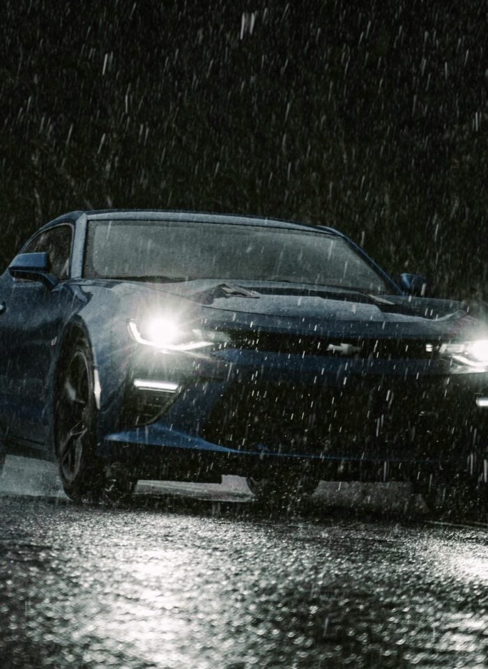 Blue sports car driving through heavy rain at night with bright headlights reflecting on the wet road, capturing dramatic all-weather driving conditions and extreme weather mobility.