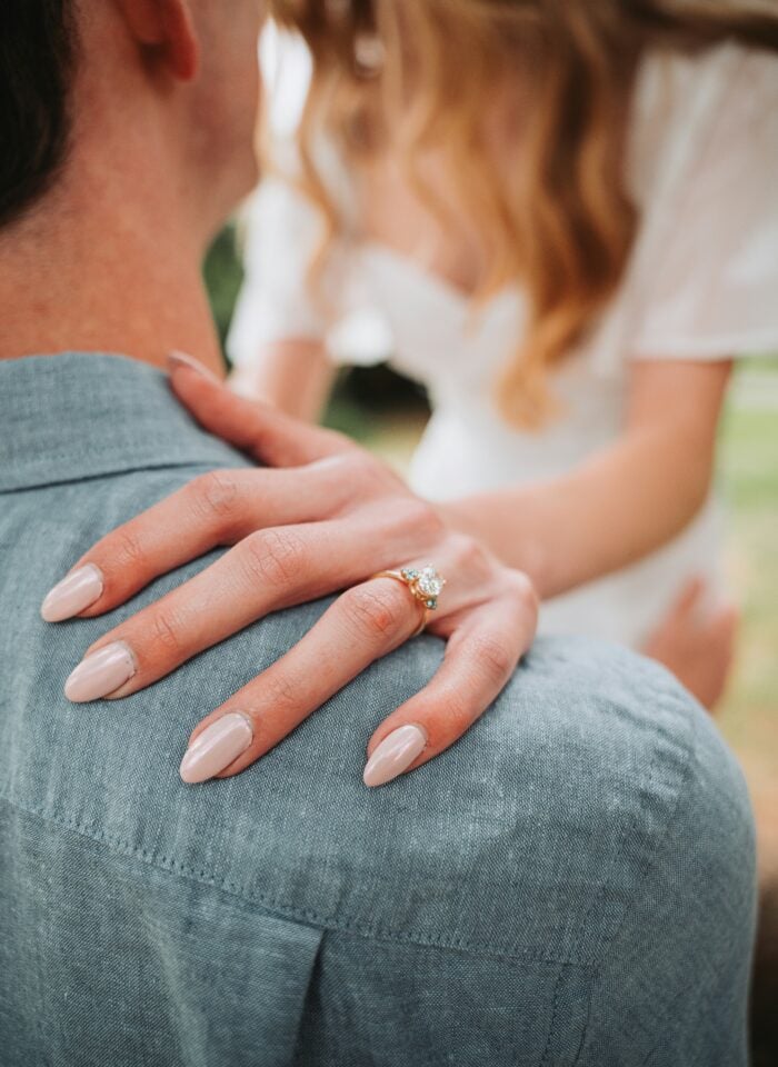Close-up of a solitaire diamond engagement ring being placed on a woman’s finger, symbolizing a romantic proposal and timeless jewelry style.