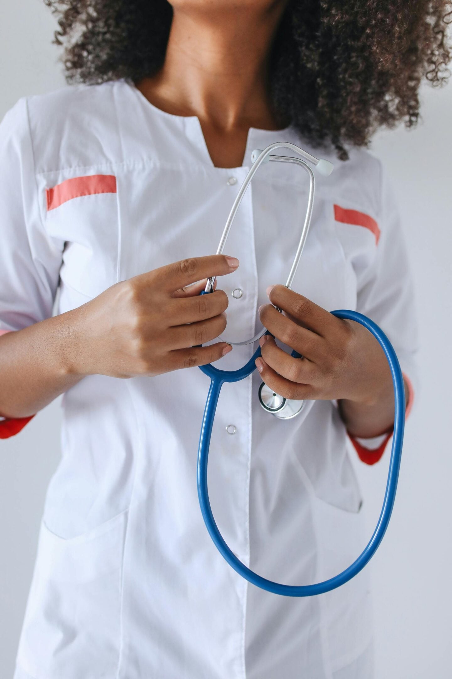 Close-up of a healthcare professional wearing a white medical uniform with red accents, holding a blue stethoscope against a neutral background.