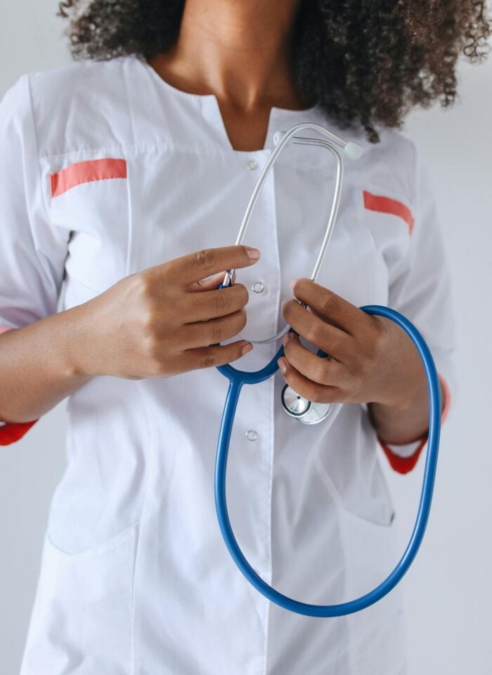 Close-up of a healthcare professional wearing a white medical uniform with red accents, holding a blue stethoscope against a neutral background.