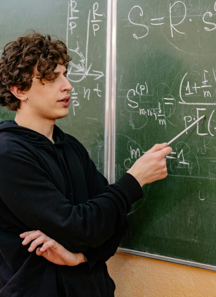 Math students solving equations and discussing formulas on a classroom chalkboard during a collaborative lesson.