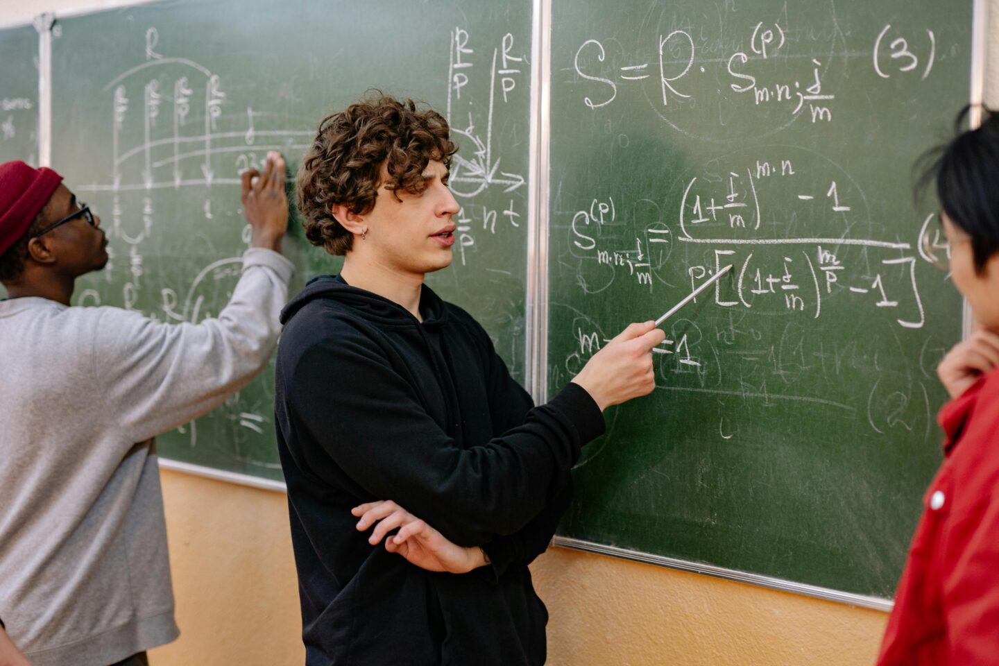 Math students solving equations and discussing formulas on a classroom chalkboard during a collaborative lesson.