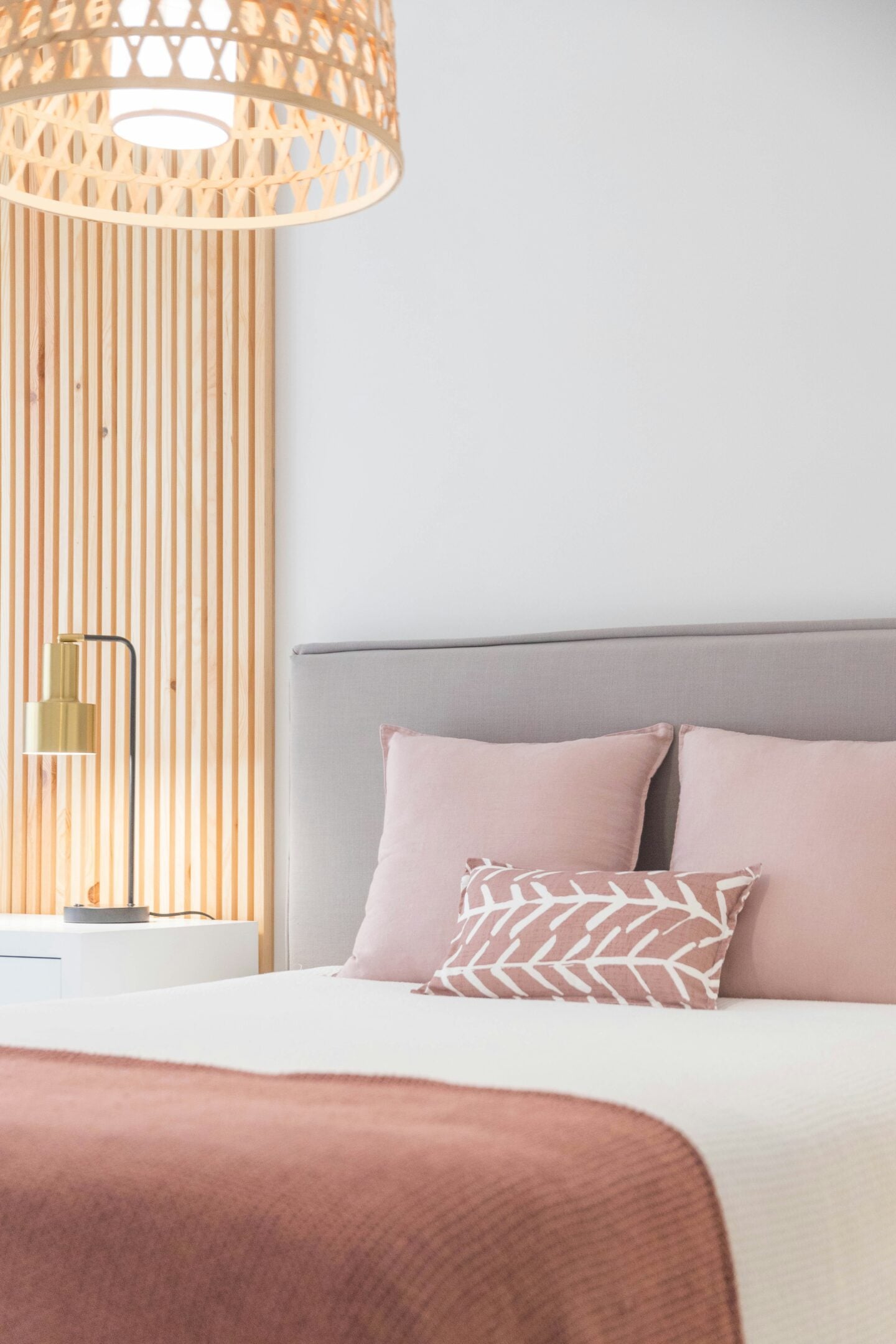 Modern minimalist bedroom with blush pink bedding, upholstered headboard, wooden wall panels, and soft ambient lighting for a cozy contemporary home decor aesthetic.