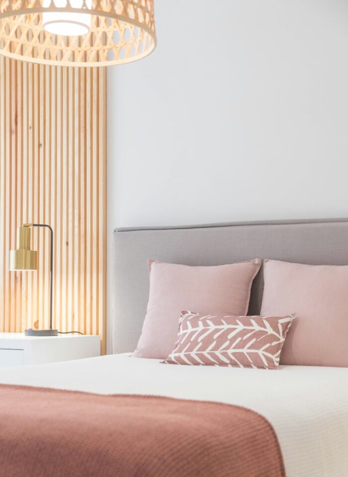 Modern minimalist bedroom with blush pink bedding, upholstered headboard, wooden wall panels, and soft ambient lighting for a cozy contemporary home decor aesthetic.