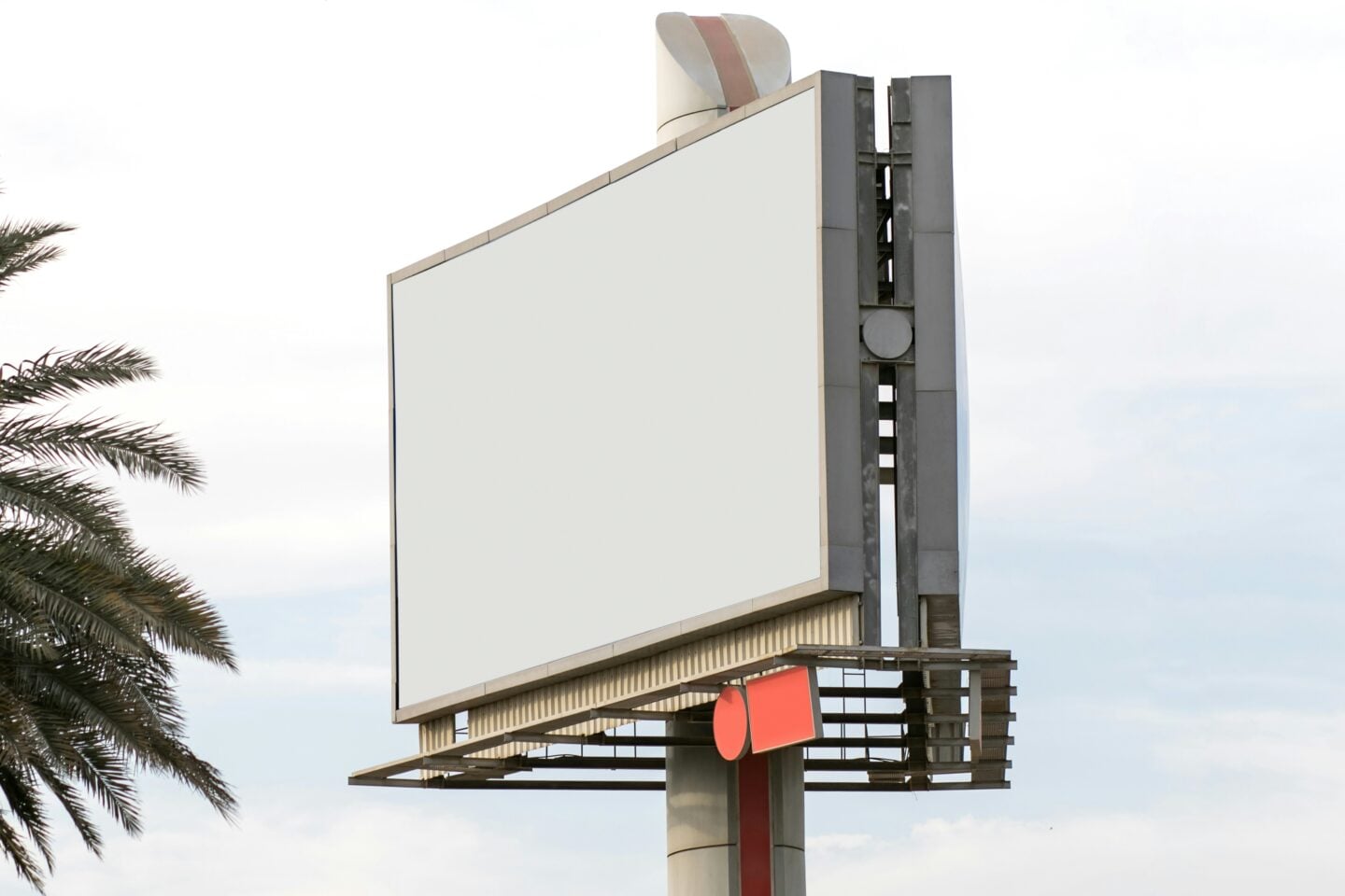Large empty outdoor billboard sign for marketing and advertising beside palm trees under a bright sky