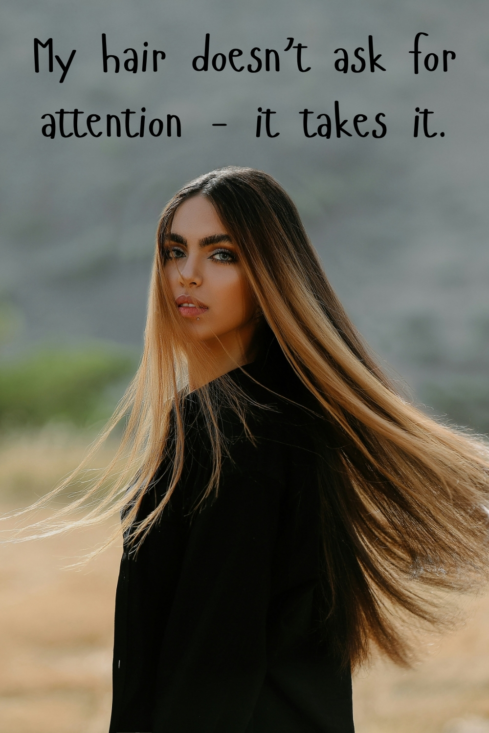 Woman with long sleek ombre hair outdoors looking over her shoulder with the quote “My hair doesn’t ask for attention – it takes it.”