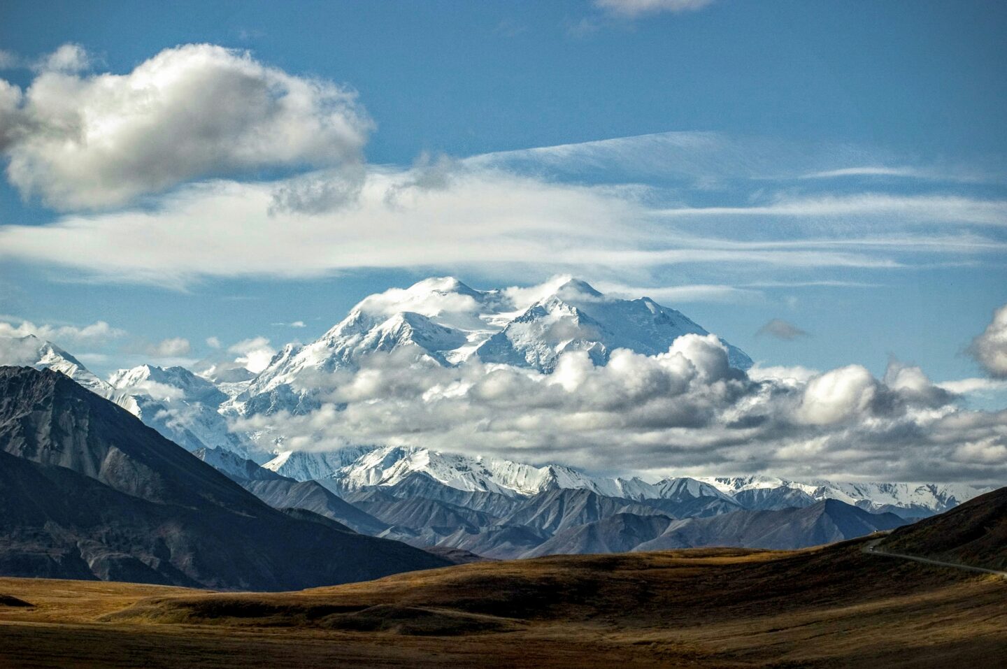 Denali, Alaska, USA: Snow-covered Denali rises above rugged mountain ranges and rolling tundra beneath dramatic clouds in Alaska's wilderness.