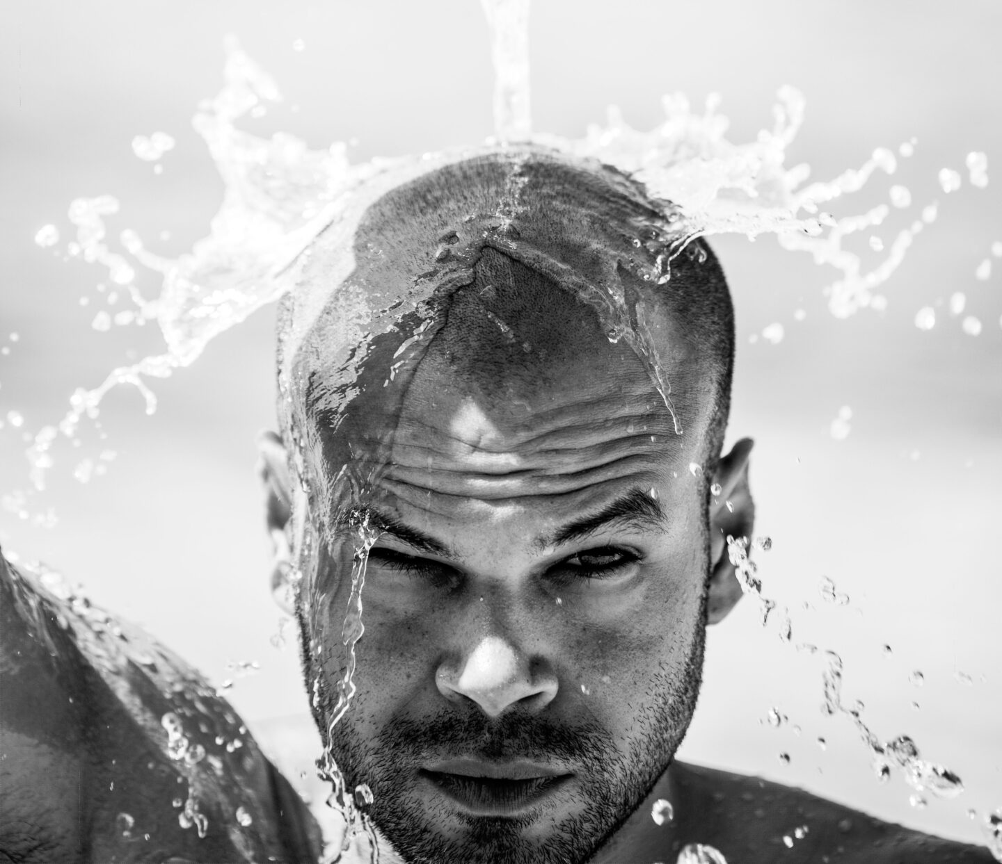 A man splashing water over his freshly shaved head.