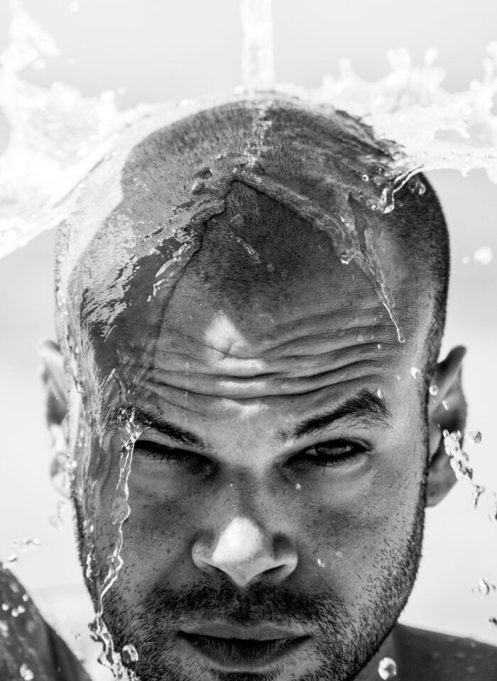 A man splashing water over his freshly shaved head.