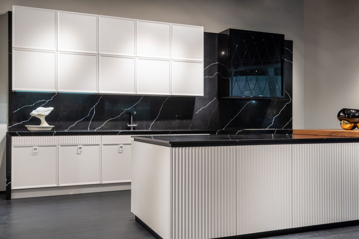 Modern kitchen featuring extensive built-in storage, including floor-to-ceiling white cabinets, a large fluted island with concealed storage, and sleek black marble-effect countertops and backsplash.
