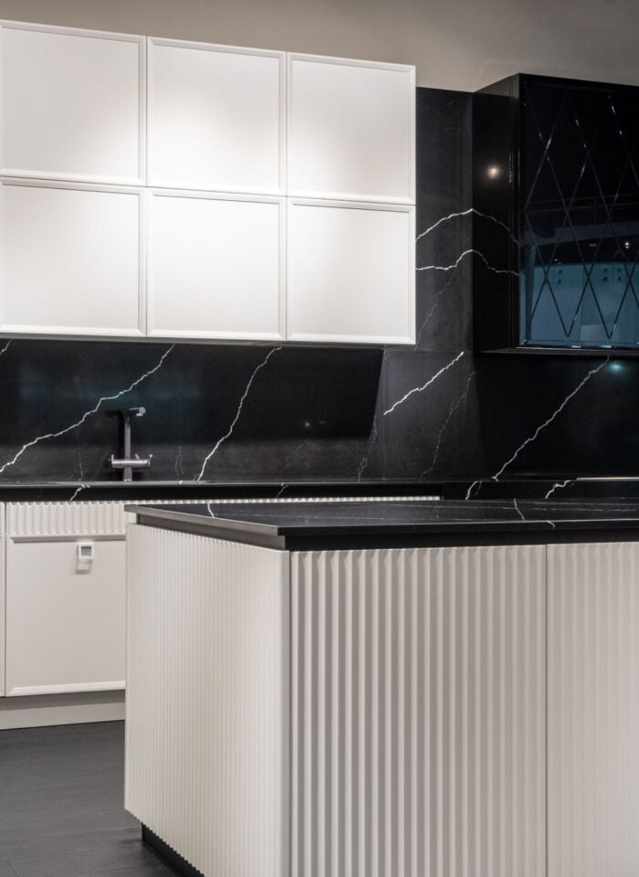 Modern kitchen featuring extensive built-in storage, including floor-to-ceiling white cabinets, a large fluted island with concealed storage, and sleek black marble-effect countertops and backsplash.