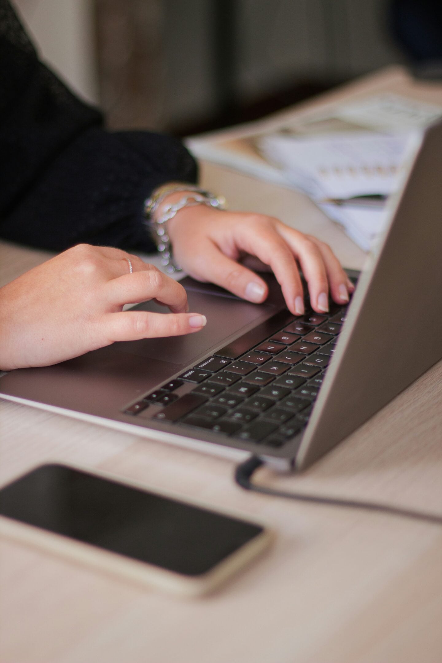 Close-up of a person typing on a laptop at a desk with a smartphone nearby, illustrating email marketing, digital communication, and online business management.