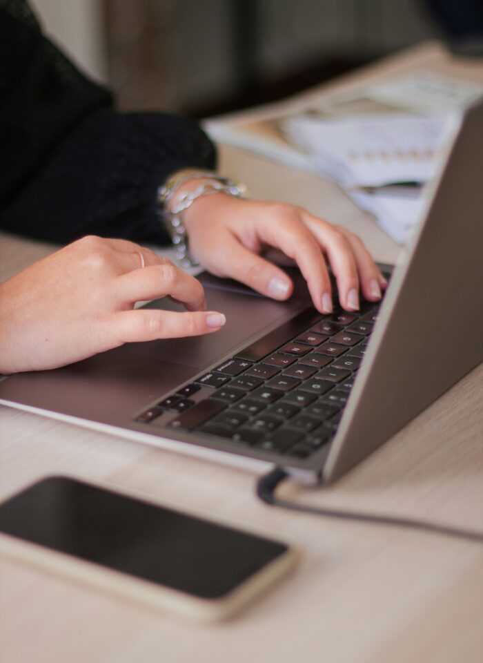 Close-up of a person typing on a laptop at a desk with a smartphone nearby, illustrating email marketing, digital communication, and online business management.