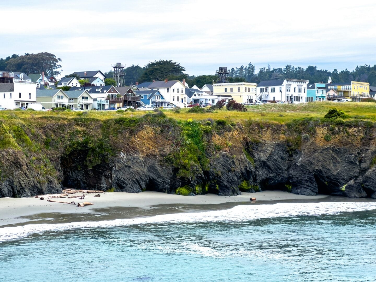 Coastal cliffs and shoreline with colorful buildings overlooking the Pacific Ocean in Mendocino, California, USA.