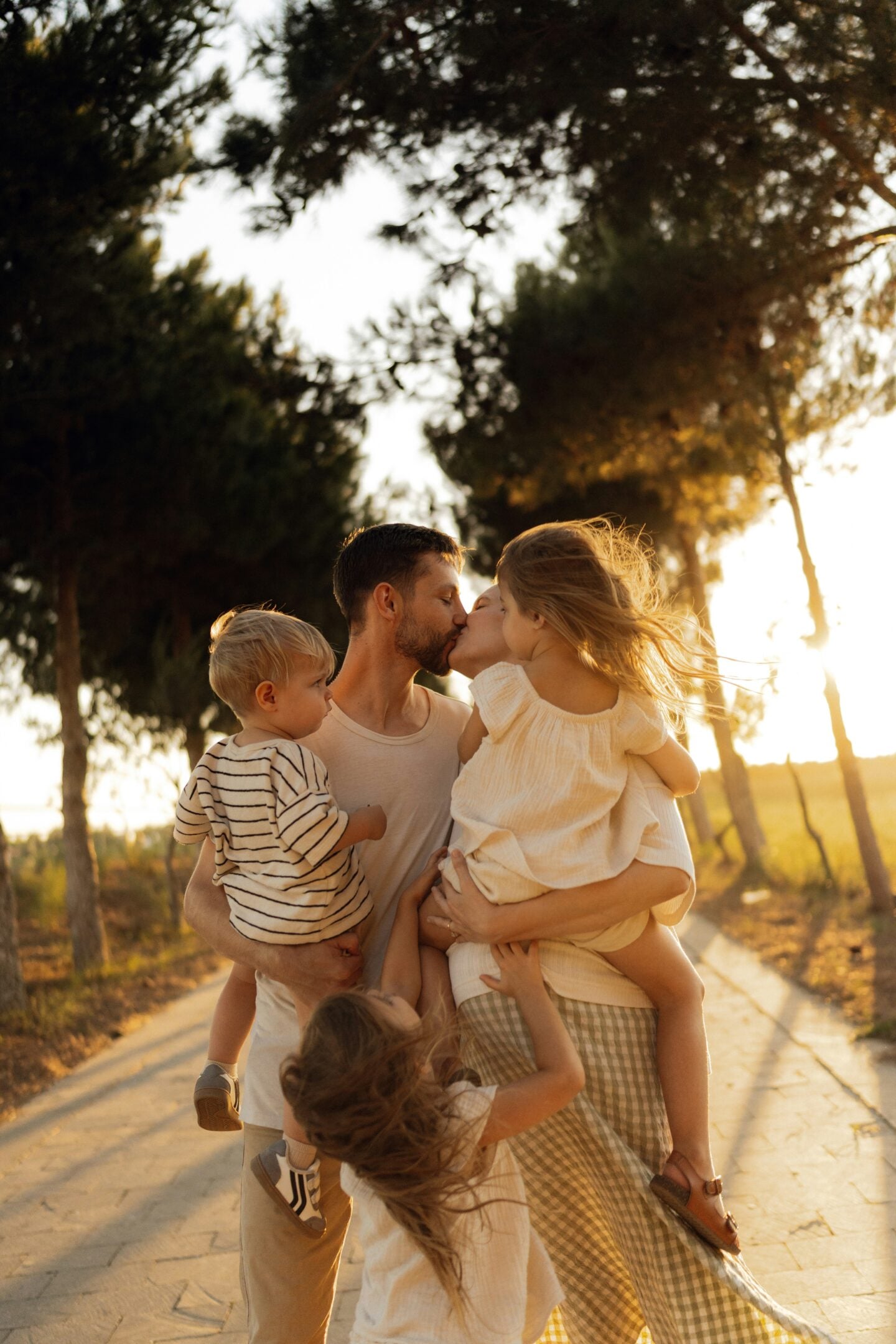 Parents sharing a kiss while holding their children during a sunset walk.