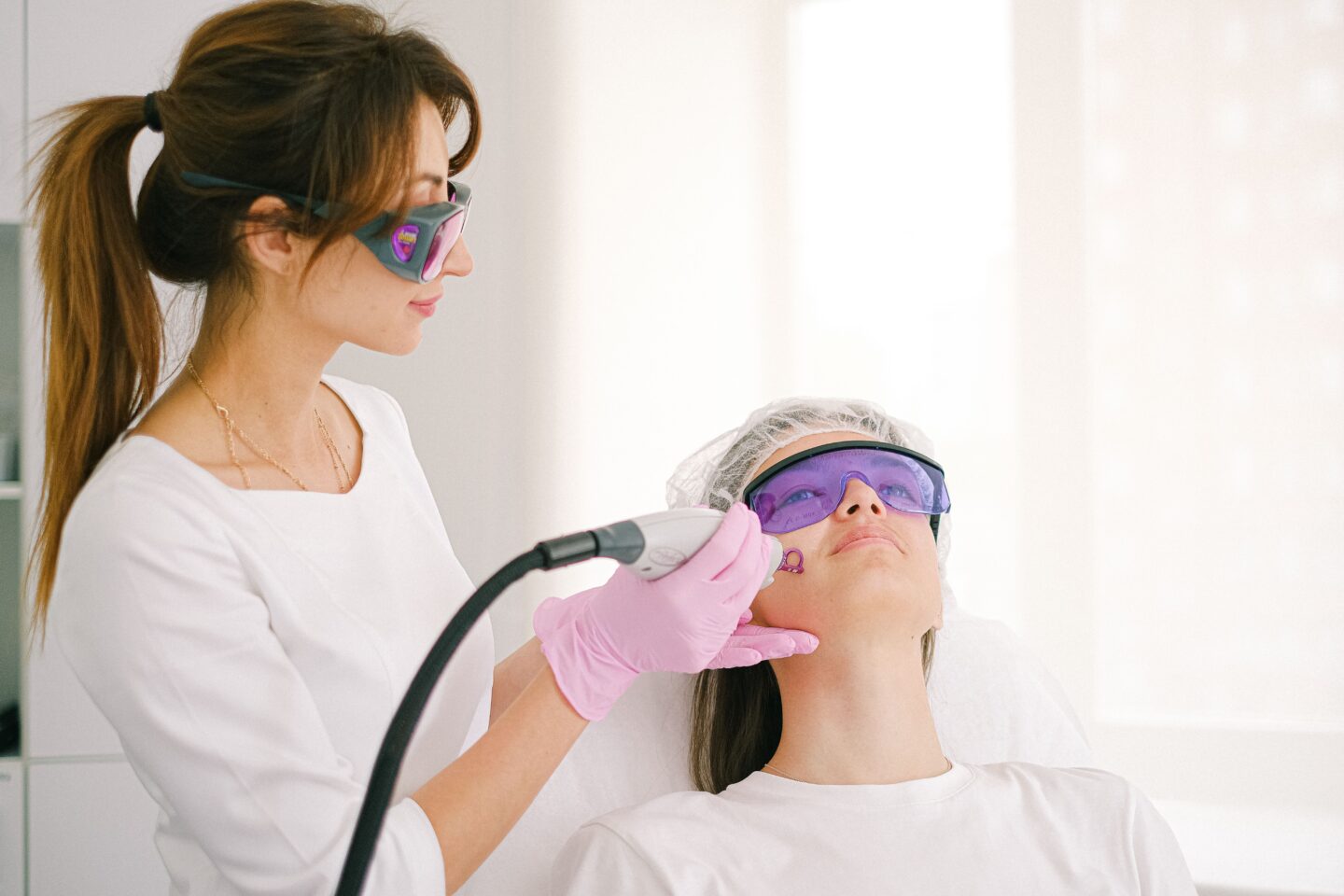Woman receiving a non-invasive laser facial treatment at a modern aesthetic clinic while wearing protective eyewear.