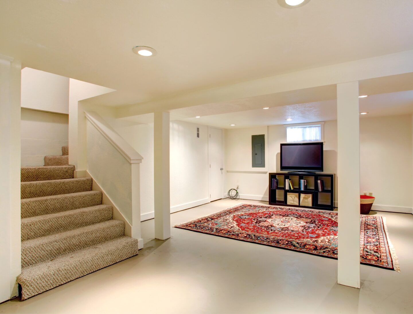Finished basement with carpeted stairs, recessed lighting, a seating area with a TV, and an open layout showcasing a comfortable, renovated living space.