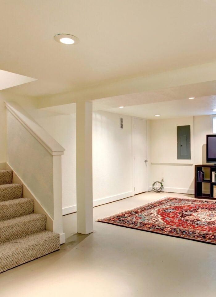 Finished basement with carpeted stairs, recessed lighting, a seating area with a TV, and an open layout showcasing a comfortable, renovated living space.