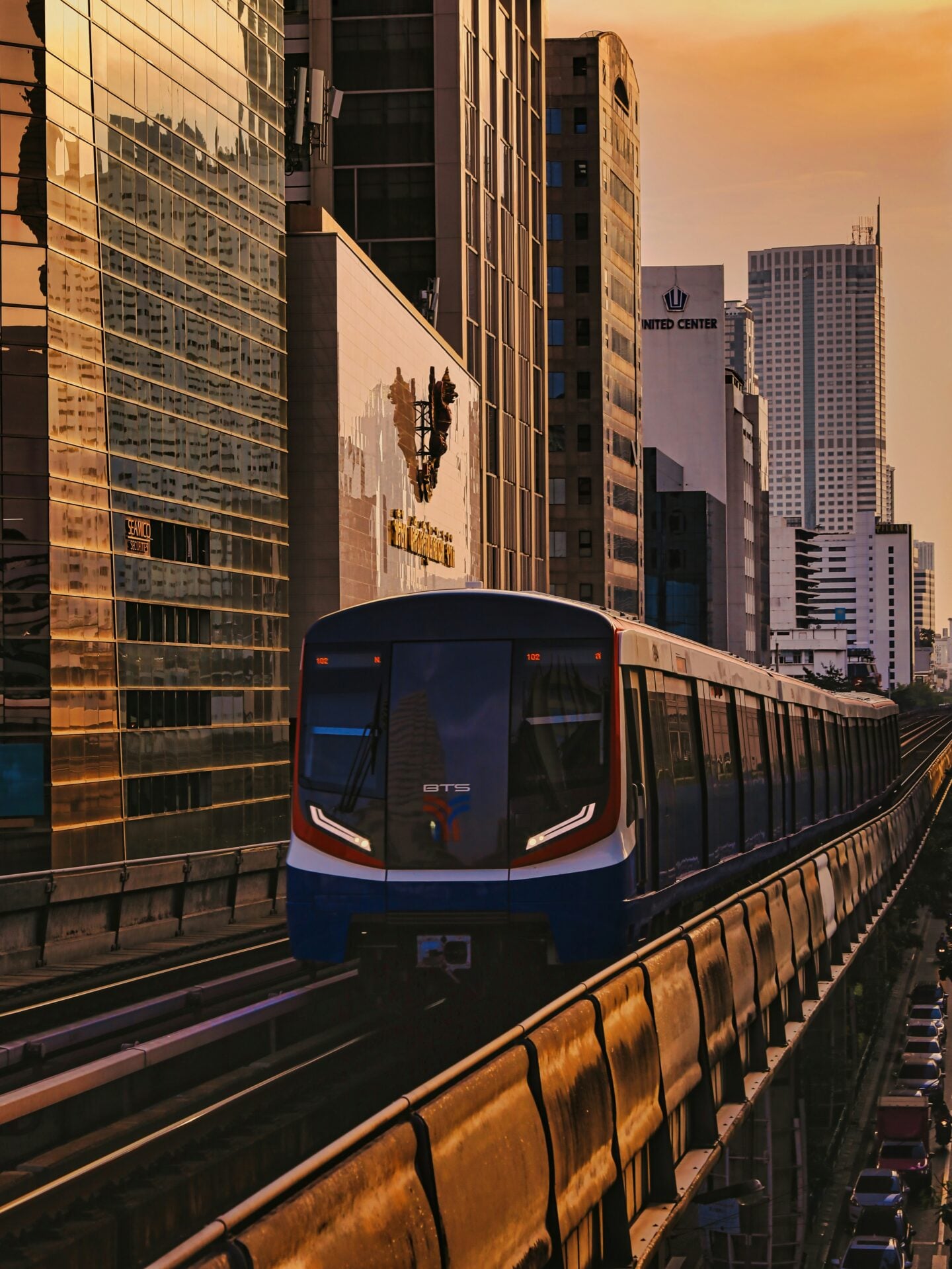 BTS Skytrain travelling through central Bangkok at sunset with modern skyscrapers in the background.