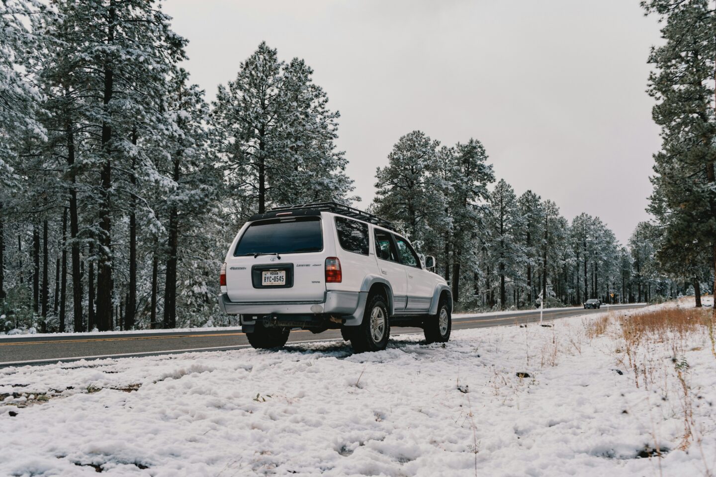 White SUV with a roof rack parked beside a snow-covered forest road, illustrating a vehicle prepared for road trips and outdoor adventures.