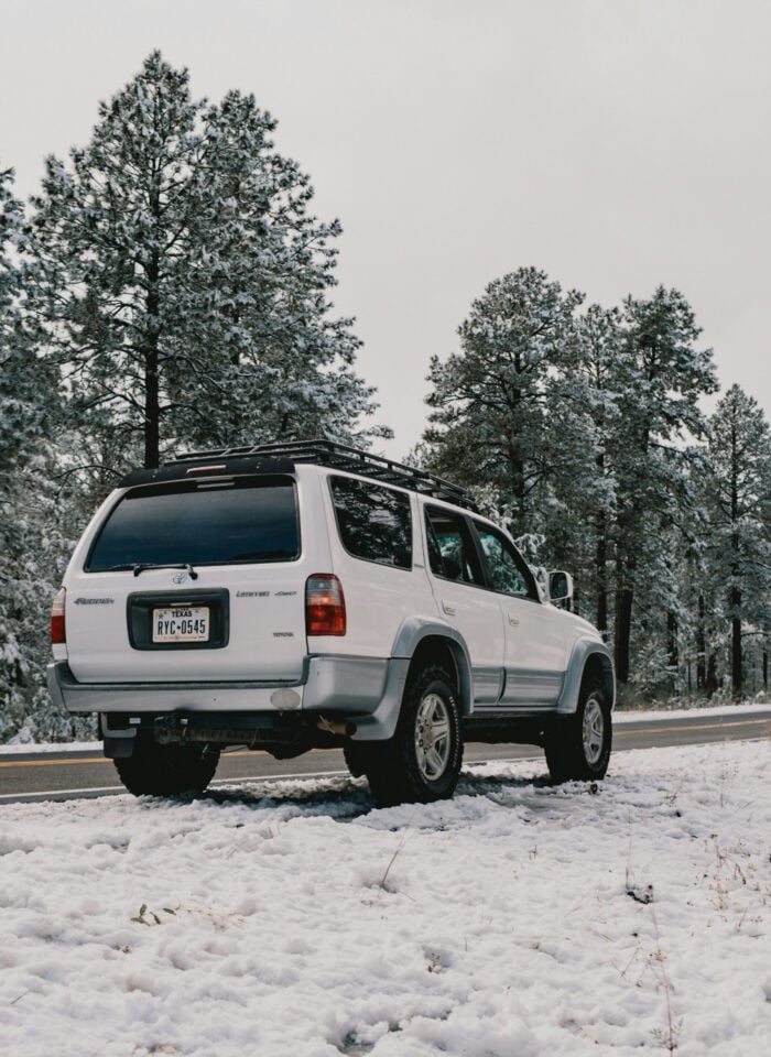 White SUV with a roof rack parked beside a snow-covered forest road, illustrating a vehicle prepared for road trips and outdoor adventures.