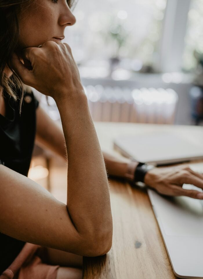 Woman reviewing her finances while working on a laptop at a wooden desk.